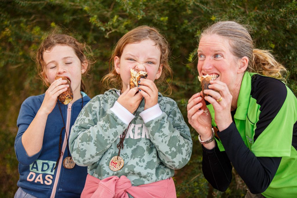 3 people smiling as they eat their damper